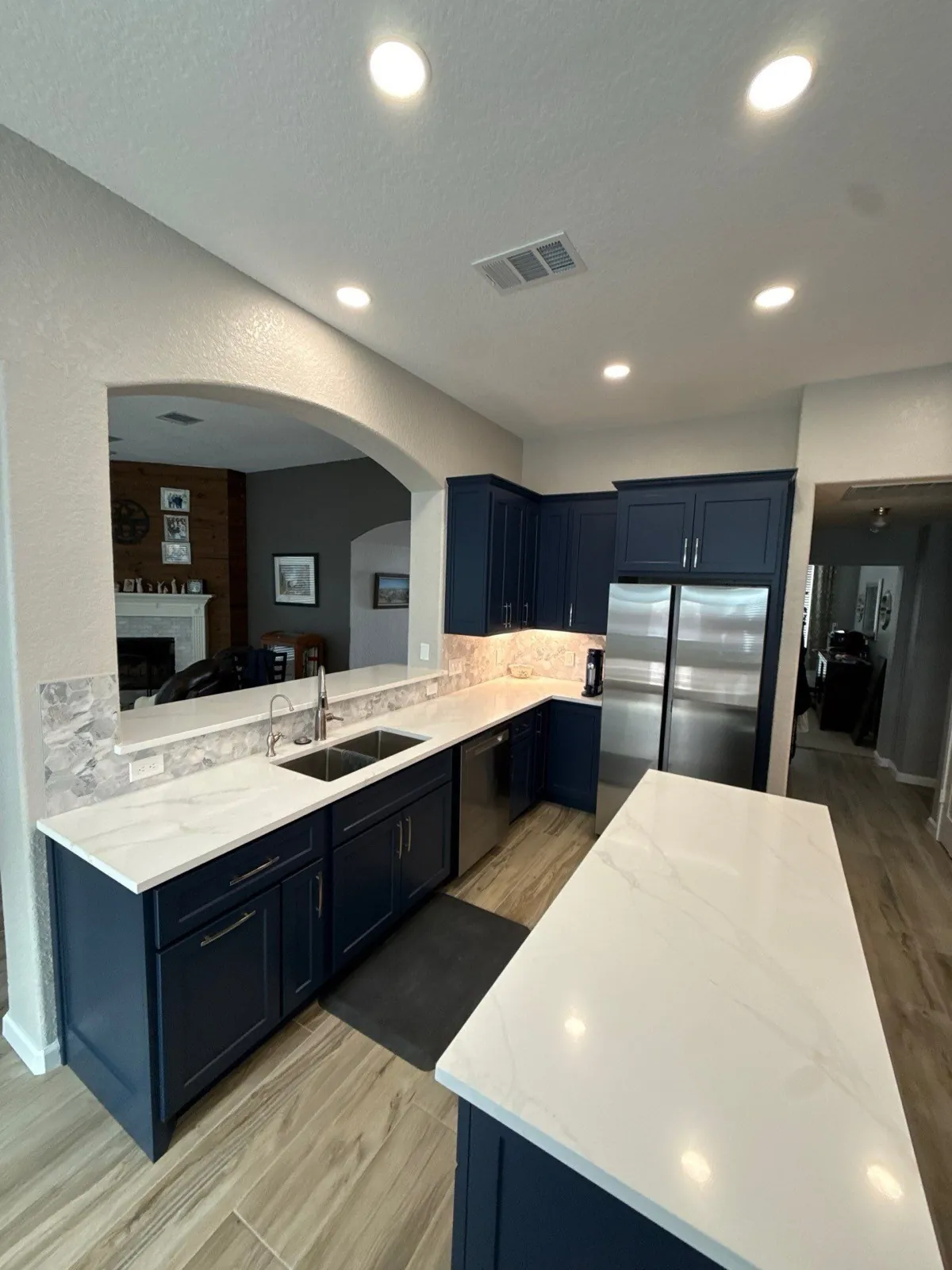 Finished kitchen with navy shaker cabinets, white quartz counters and recessed ceiling lights