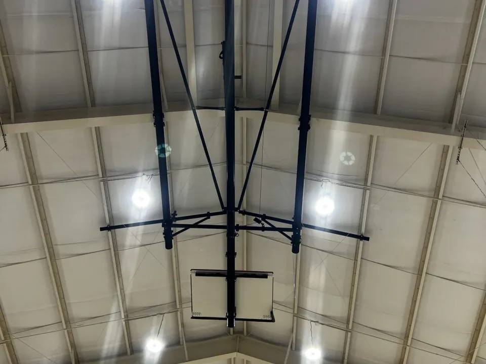 High-bay light fixtures in a gymnasium ceiling, with a basketball goal