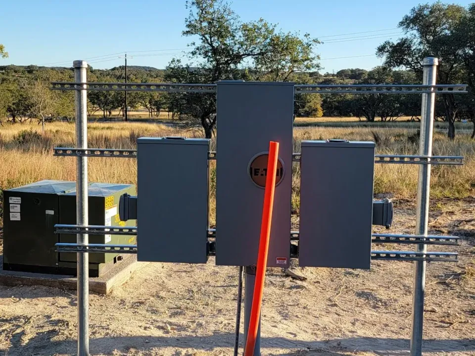 Outdoor meter base and electrical panels mounted on a pedestal beside a pad-mount transformer on a rural lot