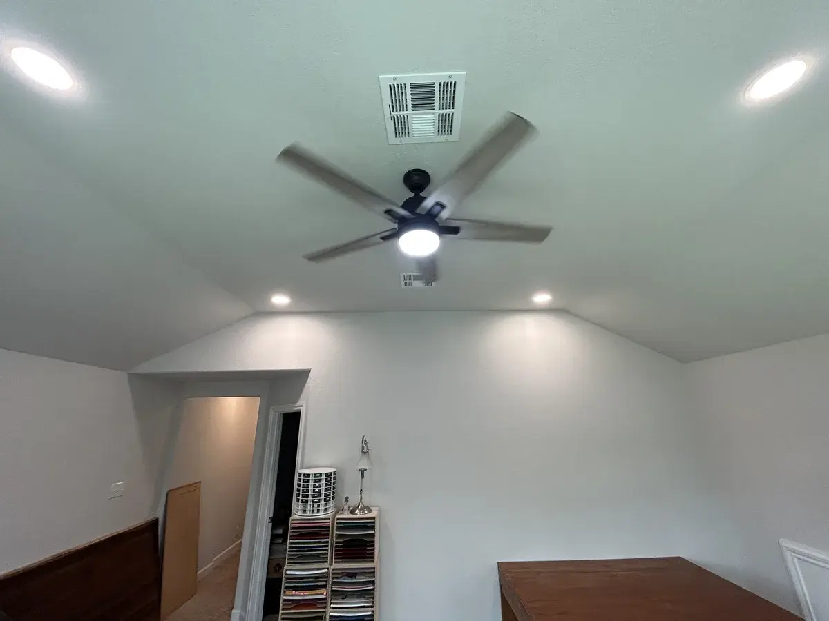 A ceiling fan with a light kit between recessed lights in a vaulted room
