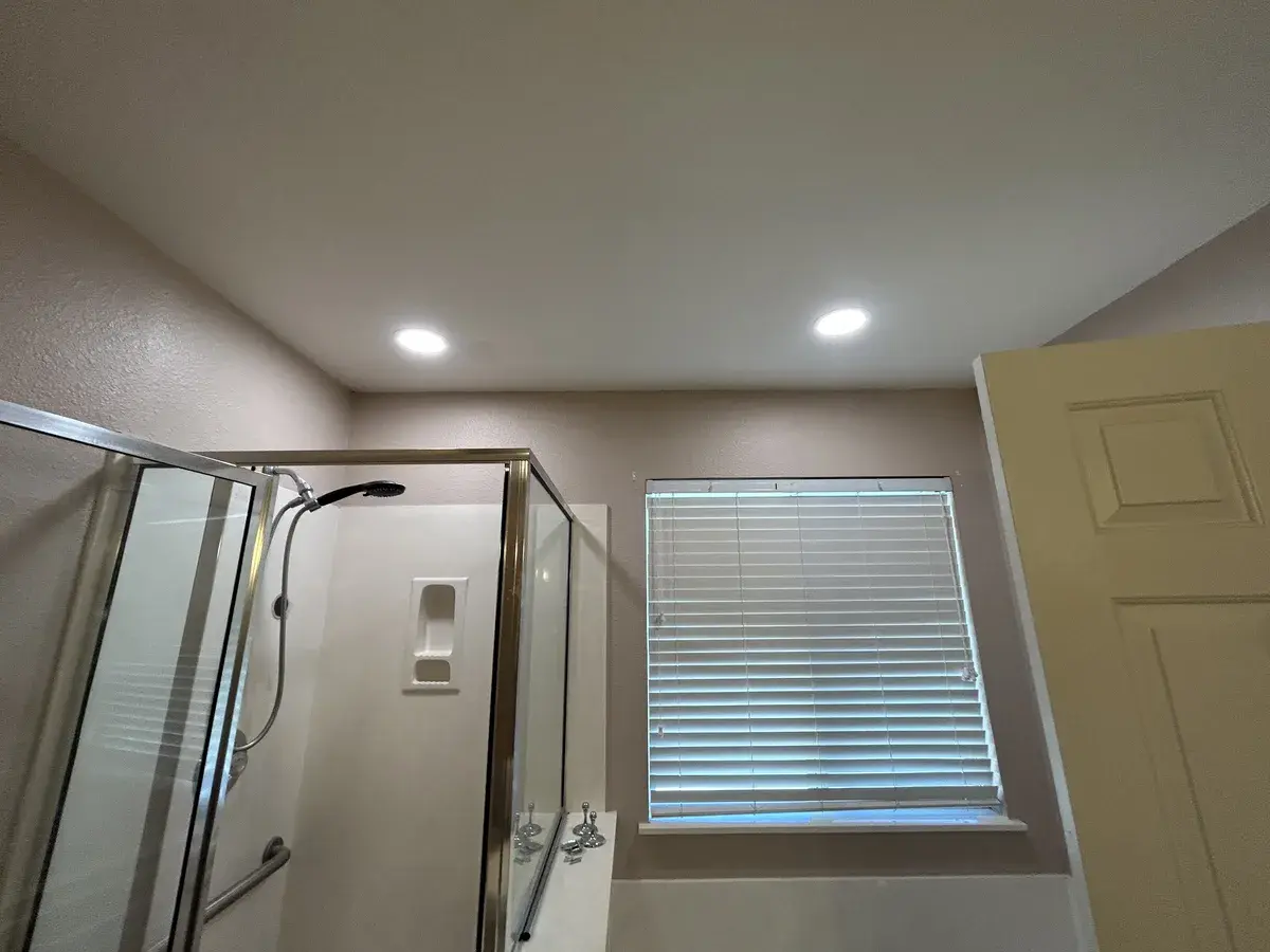 Two recessed LED lights in the ceiling above a shower and window in a remodeled bathroom